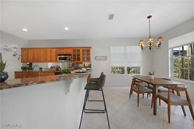 kitchen featuring light tile patterned flooring, a breakfast bar, decorative light fixtures, a notable chandelier, and light stone countertops