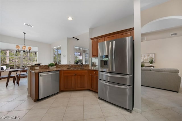 kitchen with appliances with stainless steel finishes, sink, dark stone countertops, hanging light fixtures, and kitchen peninsula