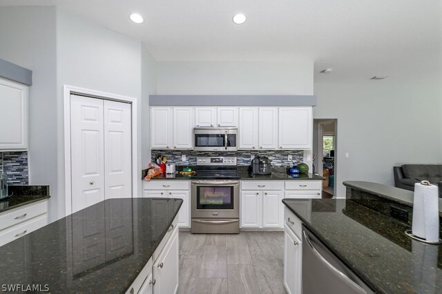 kitchen featuring white cabinetry, dark stone countertops, a high ceiling, backsplash, and stainless steel appliances