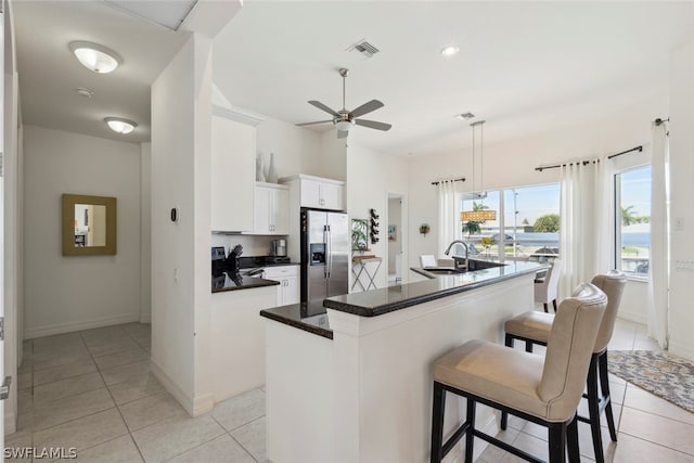 kitchen featuring pendant lighting, stainless steel fridge with ice dispenser, a kitchen island with sink, ceiling fan, and white cabinets