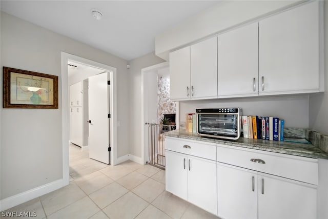 kitchen with light tile patterned flooring, white cabinets, and light stone counters