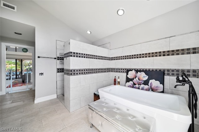 bathroom featuring tile patterned floors, lofted ceiling, a washtub, and tile walls