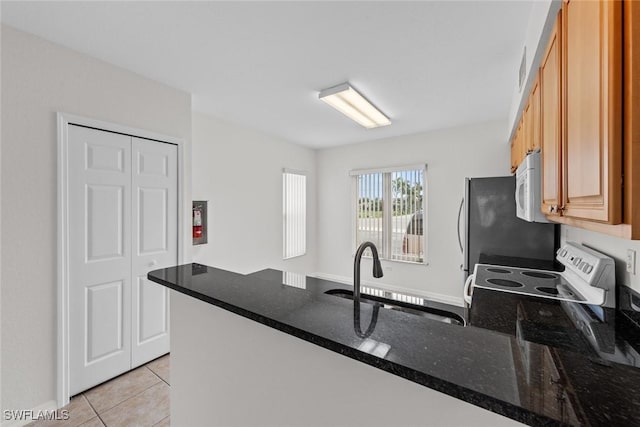 kitchen with a peninsula, white microwave, light tile patterned floors, and a sink