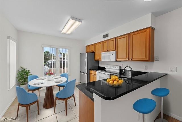 kitchen featuring a peninsula, white appliances, visible vents, brown cabinets, and dark countertops