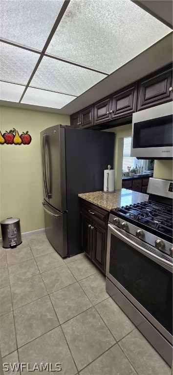 kitchen with appliances with stainless steel finishes, light stone countertops, light tile patterned floors, and dark brown cabinetry