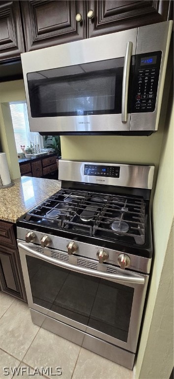 kitchen with dark brown cabinetry, light stone countertops, stainless steel appliances, and light tile patterned floors