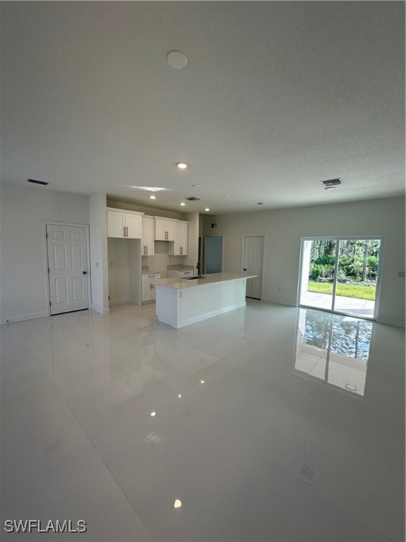 kitchen featuring a textured ceiling, sink, light tile patterned floors, white cabinets, and a center island