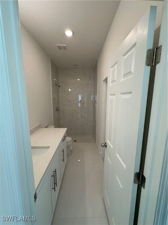 bathroom with tile patterned floors, a tile shower, vanity, a textured ceiling, and toilet