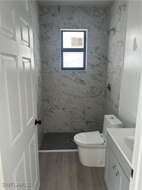 bathroom with a tile shower, vanity, wood-type flooring, and toilet