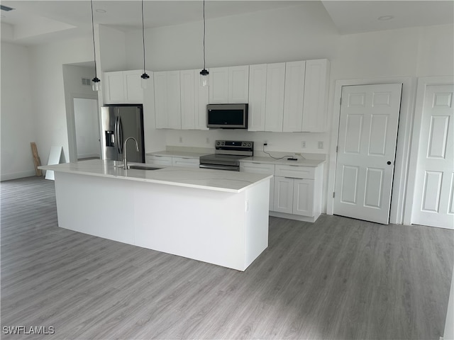 kitchen with white cabinetry, sink, stainless steel appliances, pendant lighting, and a center island with sink