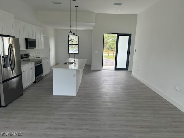 kitchen with white cabinetry, hanging light fixtures, an island with sink, light hardwood / wood-style floors, and appliances with stainless steel finishes