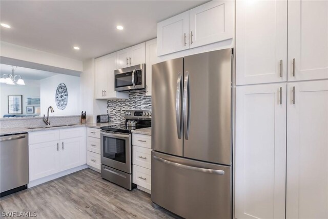 kitchen featuring stainless steel appliances, white cabinets, sink, light wood-type flooring, and light stone countertops