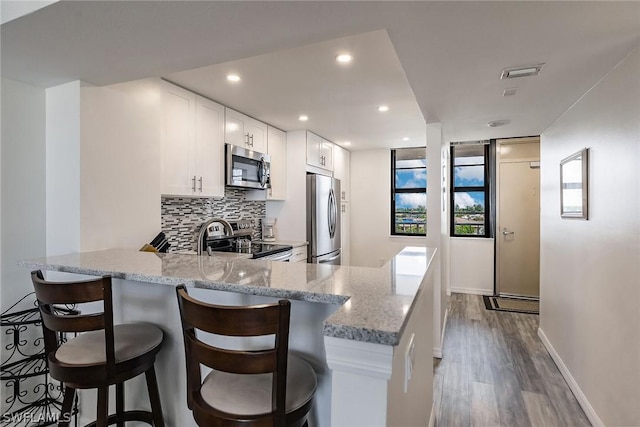 kitchen with wood finished floors, light stone countertops, stainless steel appliances, white cabinets, and tasteful backsplash