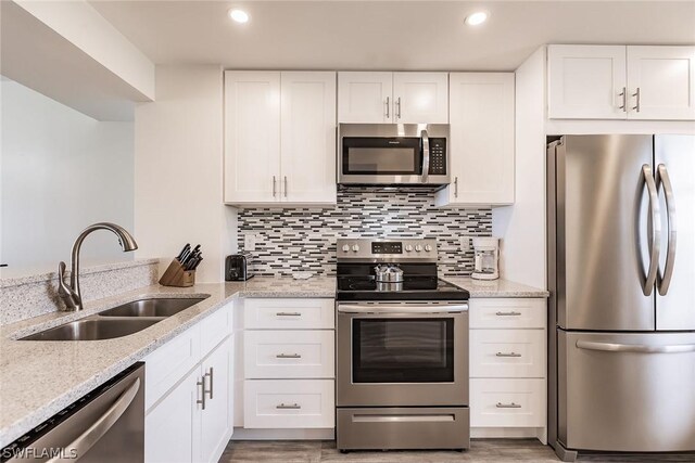 kitchen with hardwood / wood-style flooring, stainless steel appliances, white cabinets, sink, and light stone counters