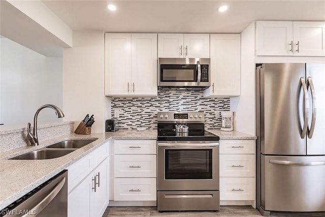 kitchen featuring light stone countertops, a sink, decorative backsplash, stainless steel appliances, and white cabinets