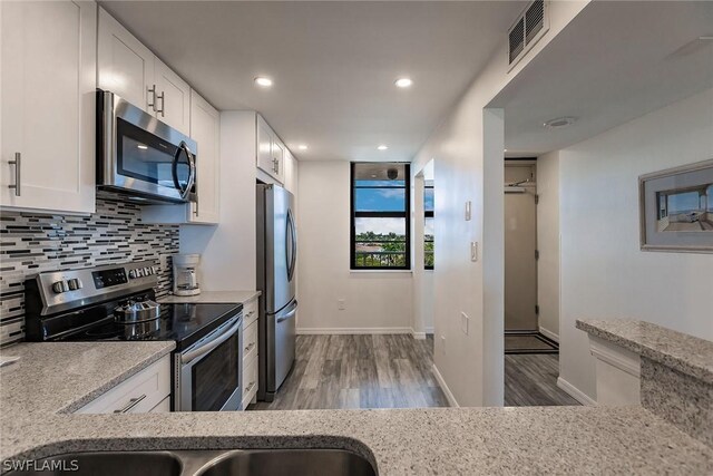 kitchen with stainless steel appliances, decorative backsplash, light wood-type flooring, light stone countertops, and white cabinetry