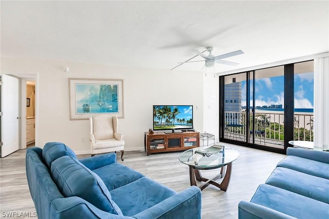 living room with a wall of windows, light wood-style flooring, a ceiling fan, and baseboards