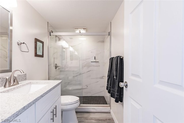 full bath with a marble finish shower, toilet, wood finished floors, and vanity