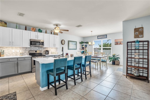 kitchen with a breakfast bar area, white cabinets, ceiling fan with notable chandelier, stainless steel appliances, and decorative backsplash