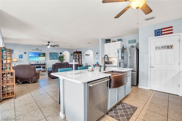 kitchen with light tile patterned floors, stainless steel appliances, a kitchen island with sink, and white cabinets