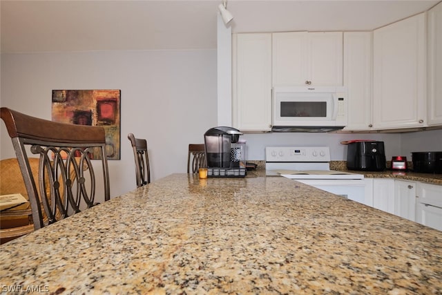 kitchen featuring white cabinets, light stone countertops, white appliances, and a kitchen bar