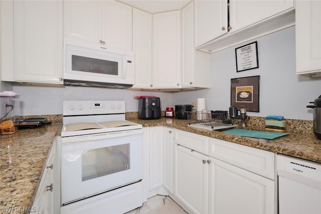 kitchen featuring light tile patterned floors, dark stone countertops, white cabinets, and white appliances