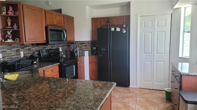 kitchen featuring dark stone counters, black appliances, sink, light tile patterned floors, and backsplash