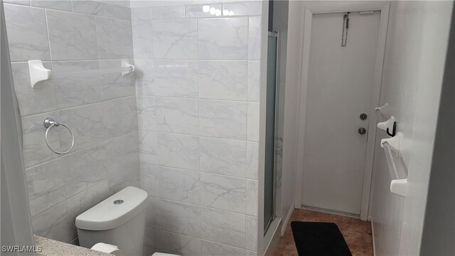 bathroom with a shower with shower door, tile walls, toilet, and tile patterned flooring