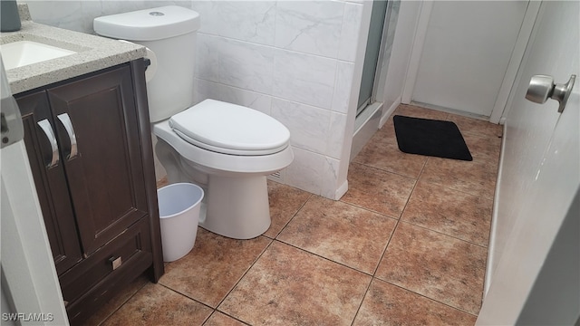 bathroom featuring a shower with door, toilet, vanity, tile walls, and tile patterned floors