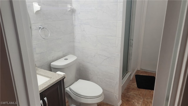 bathroom with a shower with shower door, tile walls, tile patterned flooring, toilet, and vanity