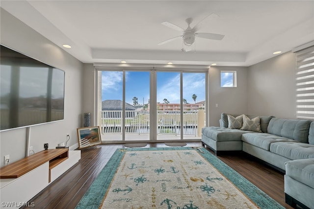 living room with ceiling fan, a tray ceiling, and dark hardwood / wood-style flooring