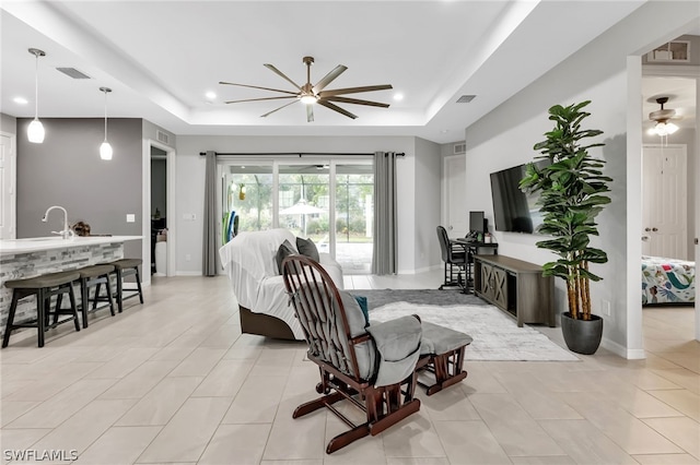 living room featuring light tile patterned flooring, ceiling fan, and a raised ceiling