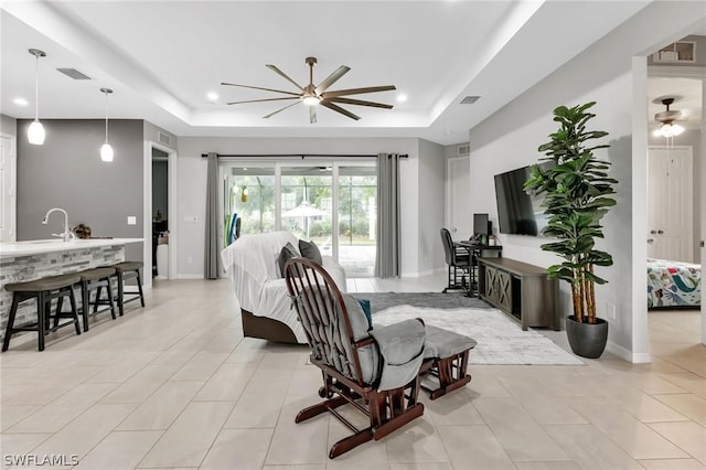 living area with a tray ceiling, recessed lighting, visible vents, and a ceiling fan