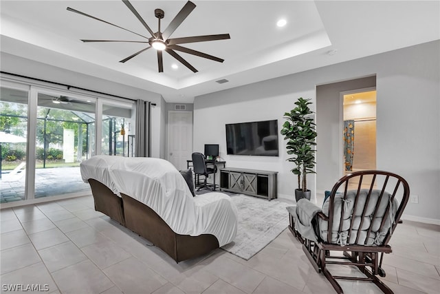 living room featuring light tile patterned floors, ceiling fan, and a tray ceiling