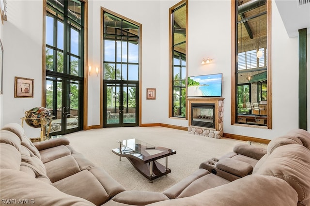 carpeted living room featuring a fireplace, french doors, a healthy amount of sunlight, and a high ceiling