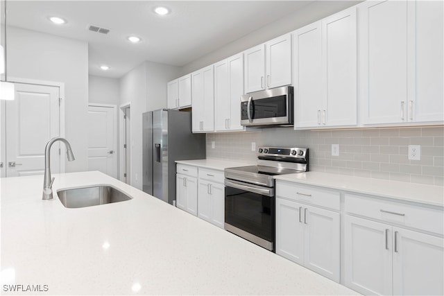 kitchen with tasteful backsplash, appliances with stainless steel finishes, sink, and white cabinets