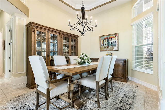 dining space with ornamental molding, a tray ceiling, a chandelier, and light tile patterned floors