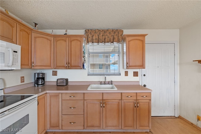 kitchen with a textured ceiling, white appliances, light wood finished floors, and a sink