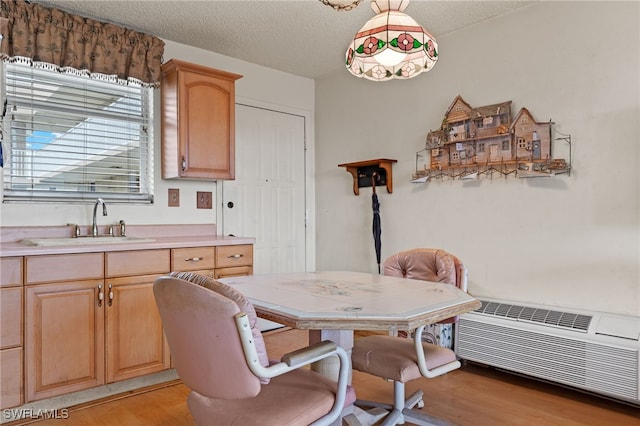 dining space with light wood-type flooring, a wall mounted air conditioner, and a textured ceiling