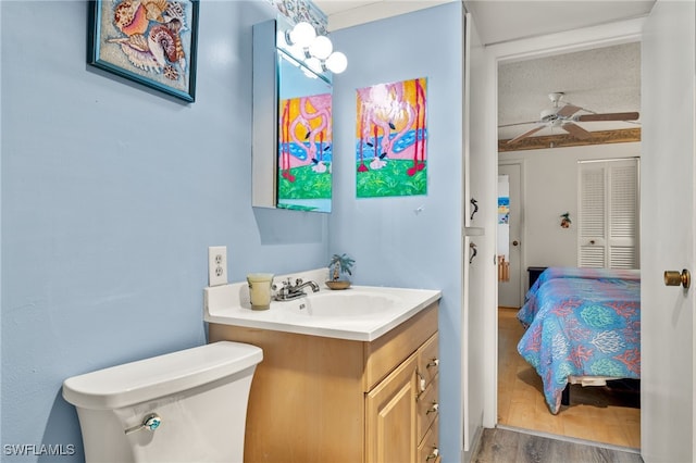 half bath with vanity, wood finished floors, a ceiling fan, and toilet