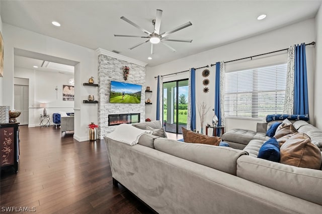 living room featuring dark hardwood / wood-style floors, a stone fireplace, ceiling fan, and crown molding