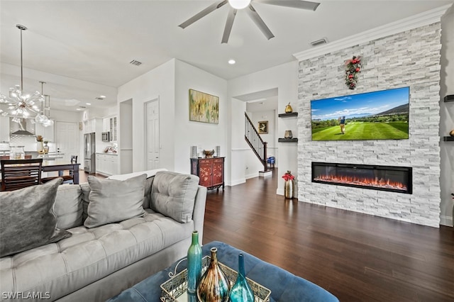 living room with a stone fireplace, dark wood-type flooring, and ceiling fan with notable chandelier