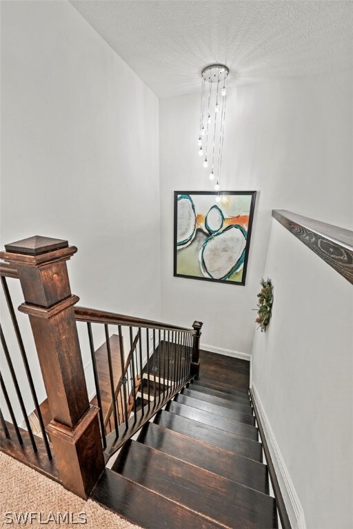 stairway with hardwood / wood-style flooring, a textured ceiling, and an inviting chandelier