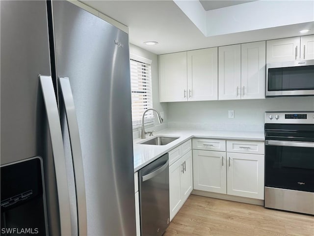 kitchen with stainless steel appliances, sink, white cabinets, and light hardwood / wood-style flooring