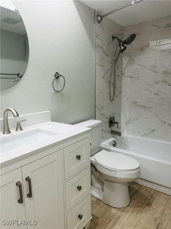 full bathroom featuring vanity, hardwood / wood-style flooring, toilet, and tiled shower / bath combo