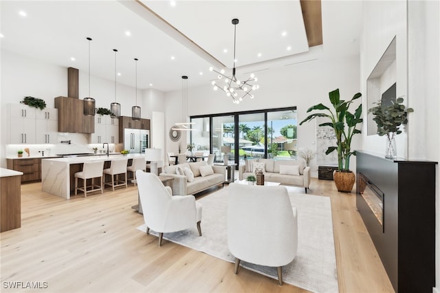 living room featuring a towering ceiling, a chandelier, sink, and light wood-type flooring