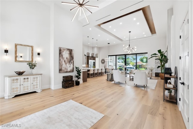 living room featuring light wood-type flooring, a chandelier, and a high ceiling