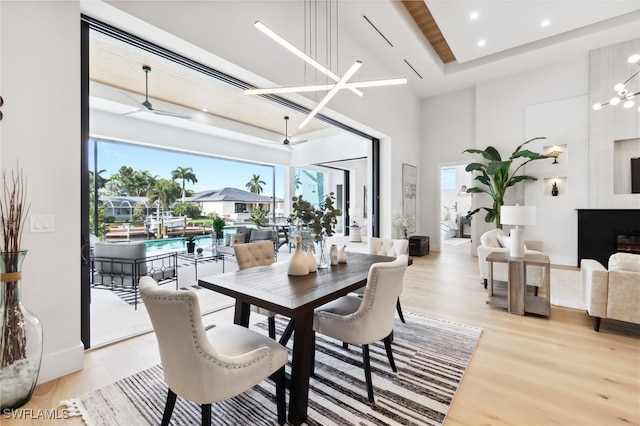 dining area featuring a towering ceiling, light hardwood / wood-style flooring, and ceiling fan with notable chandelier