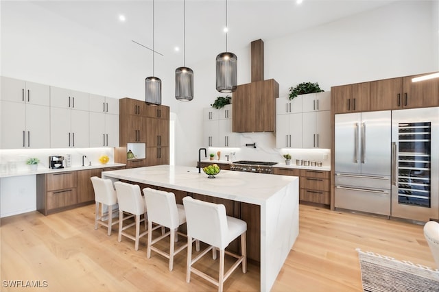 kitchen featuring white cabinetry, a towering ceiling, stainless steel appliances, and decorative light fixtures