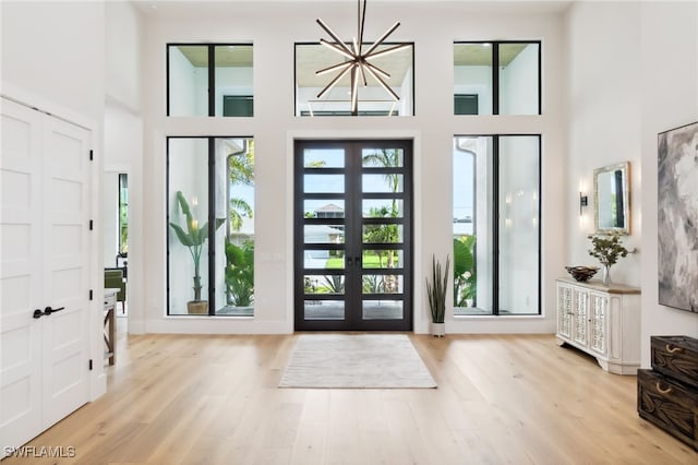 foyer with a high ceiling, an inviting chandelier, light wood-type flooring, and french doors